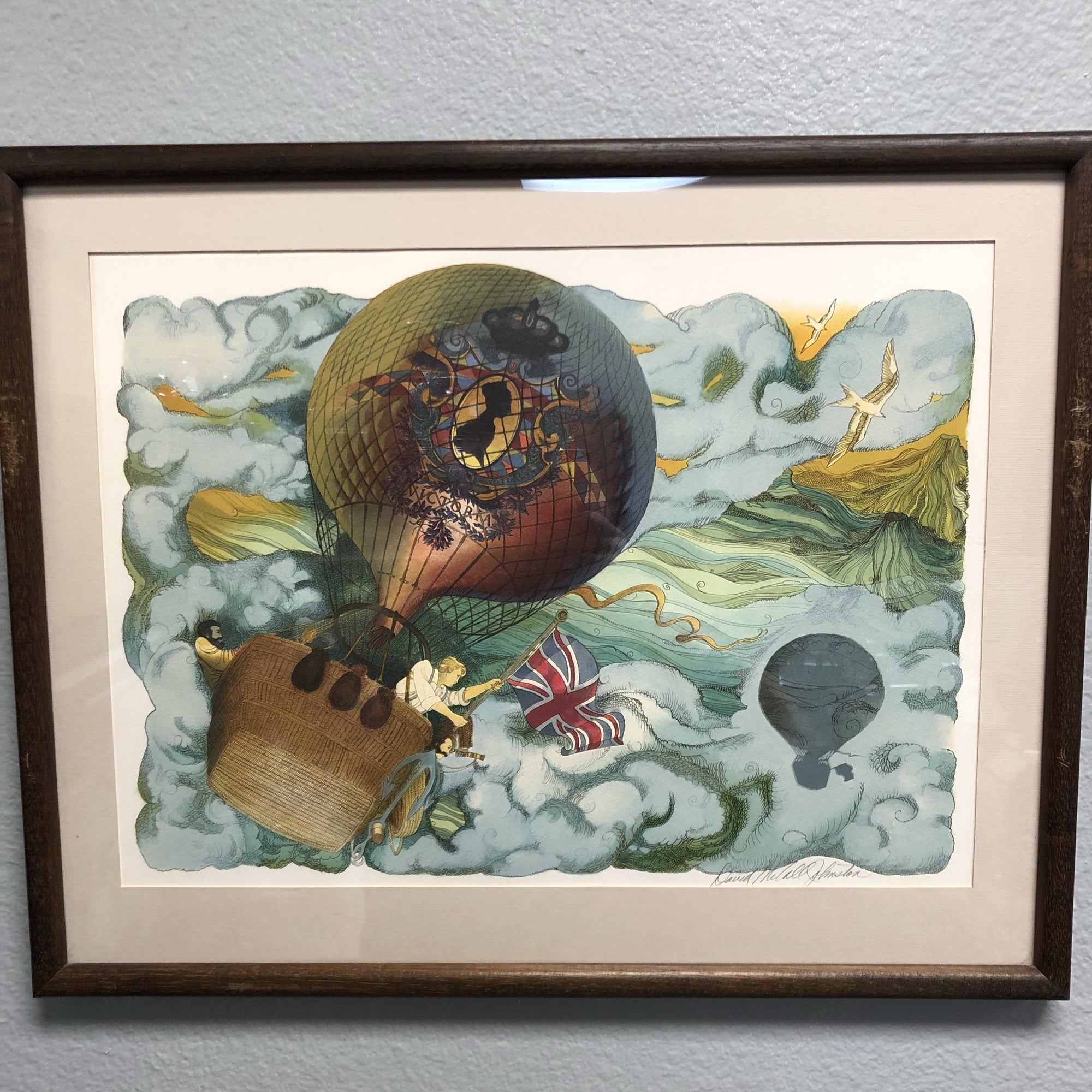A colorful original lithograph artwork depicting a whimsical scene with a hot air balloon, people, and various objects, framed in a simple brown frame.